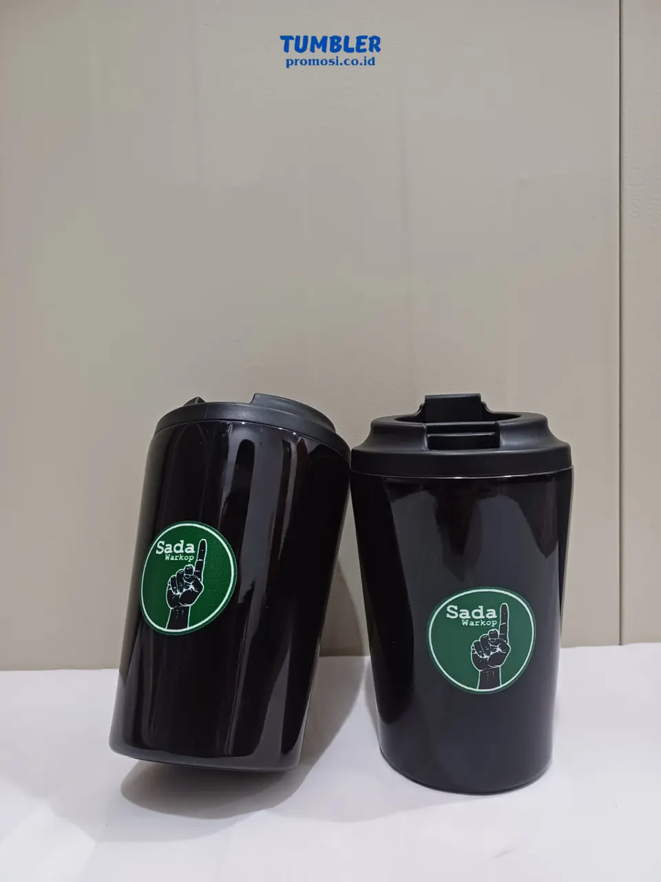 Dua mug tumbler hitam dengan desain logo hijau