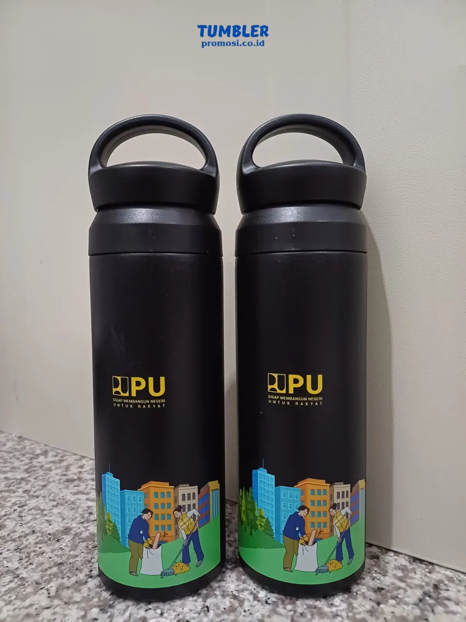 Dua botol tumbler stainless hitam dengan cetak logo dan ilustrasi berwarna